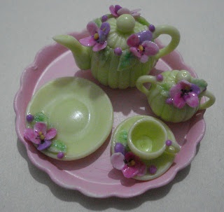 a pink and green tea set with purple flowers on the side, sitting on a pink plate