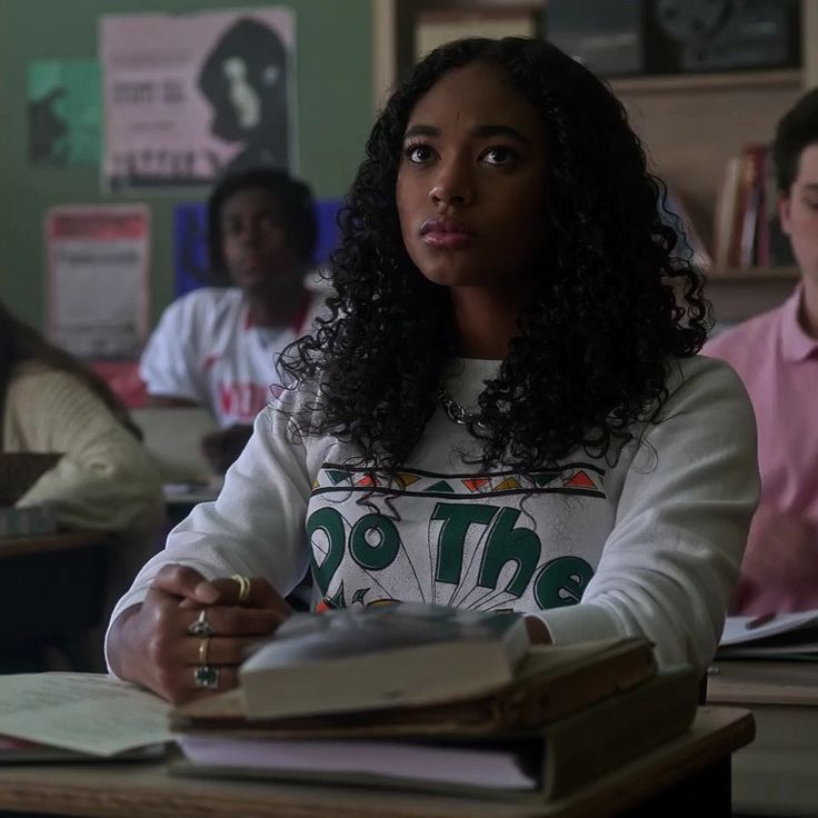 a woman sitting at a desk with books in front of her and other people behind her