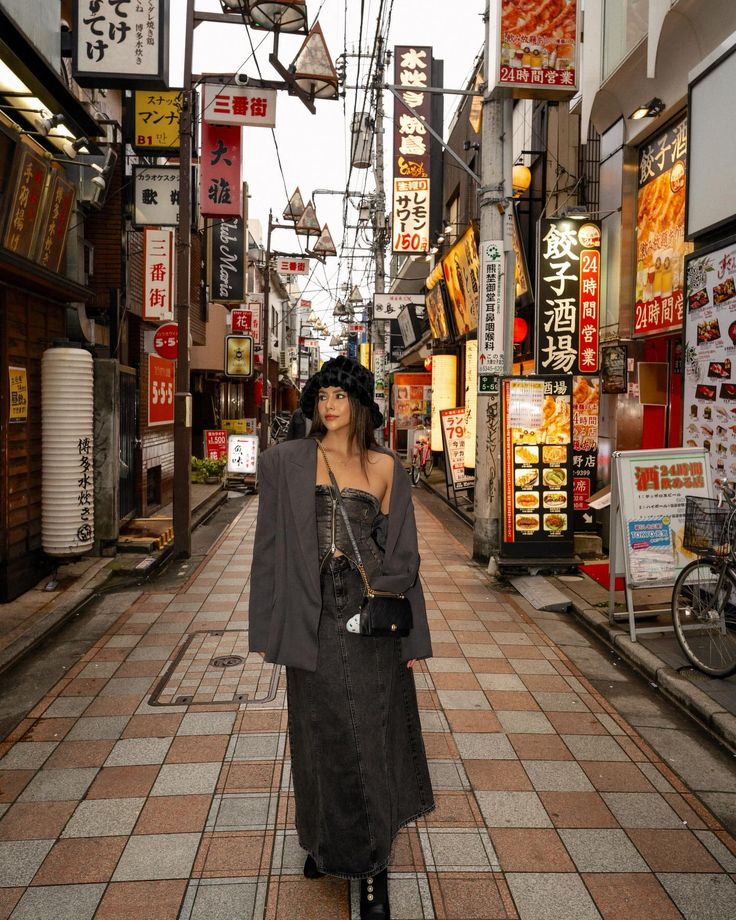 a woman is standing in an alley way wearing a hat and coat with her hands on her hips