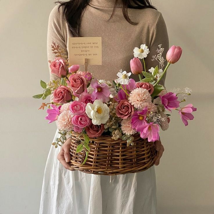 a woman holding a basket with flowers in it and a note attached to the handle