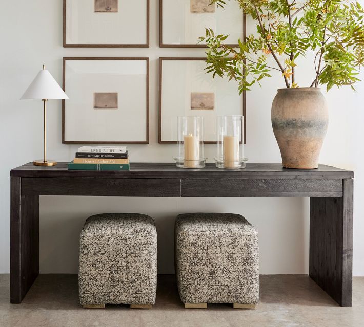 a table with two stools next to a plant and some pictures on the wall