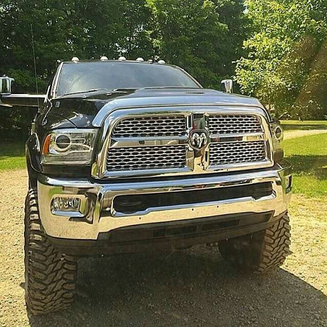 the front end of a black truck parked on top of a dirt road next to trees