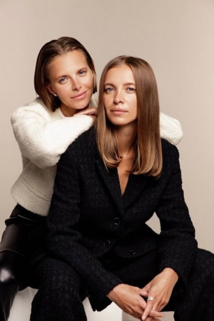 two women sitting next to each other on a white chair with their arms around one another