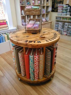 a wooden table with many different fabrics on it in a store display area next to shelves full of quilts