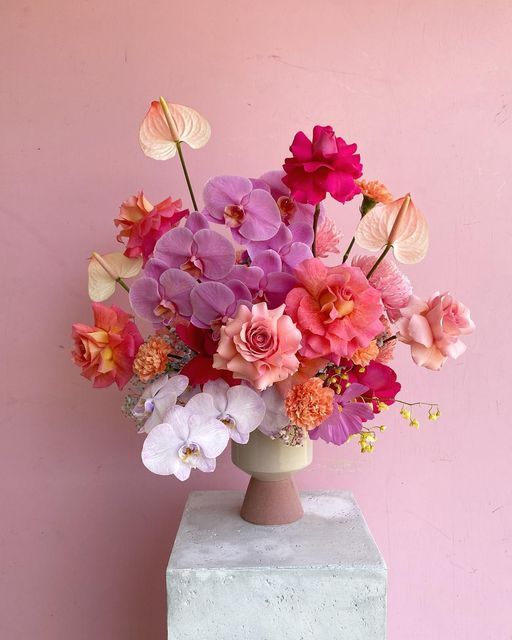 a vase filled with lots of pink and purple flowers on top of a white block