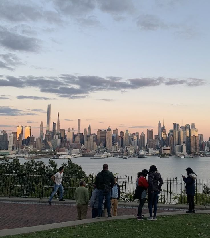 people are standing on the edge of a hill looking at the water and city in the distance