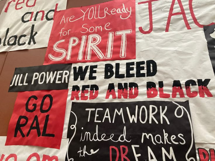 some signs are hanging on the wall in front of a brown wall with red and black writing