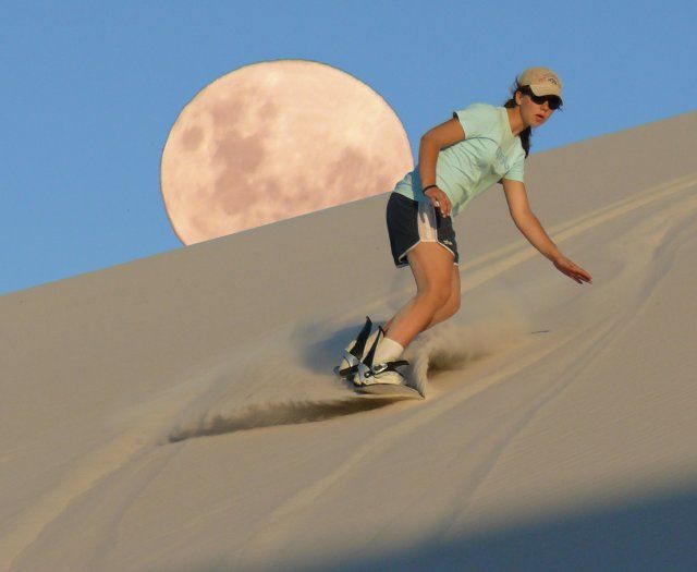 a man riding a skateboard down the side of a sand dune under a full moon