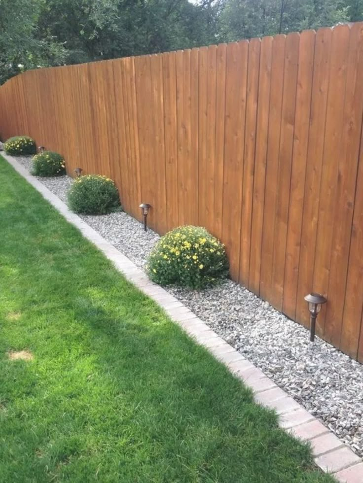 a wooden fence next to a grassy area with flowers and bushes in the corner,