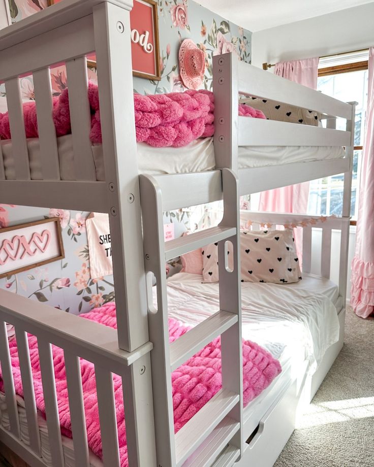 two white bunk beds with pink blankets on them in a girls'bedroom, one is made up and the other is made out of wood