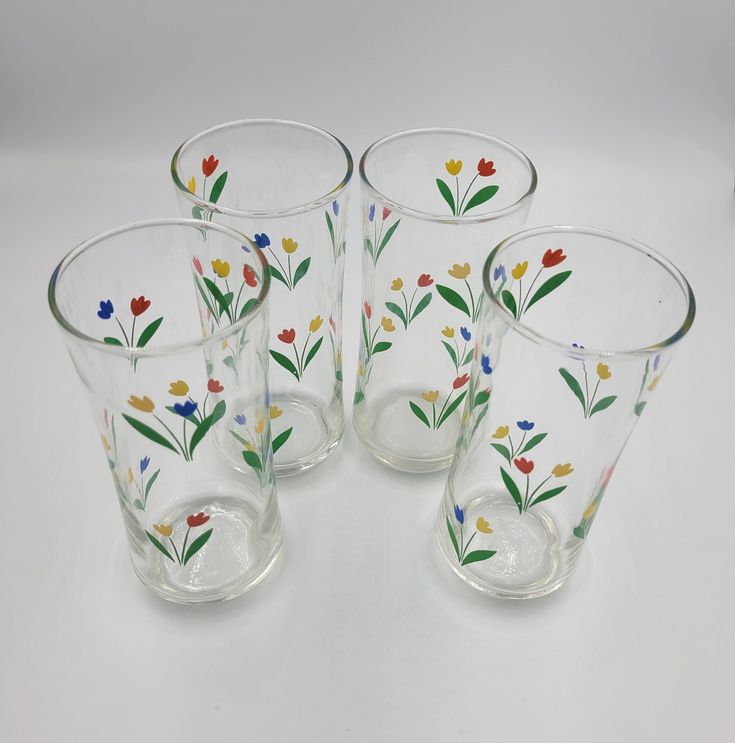 four glass cups with flowers painted on them are sitting next to each other and one is empty