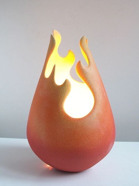 an orange vase with flames on it sitting on a white table top next to a wall