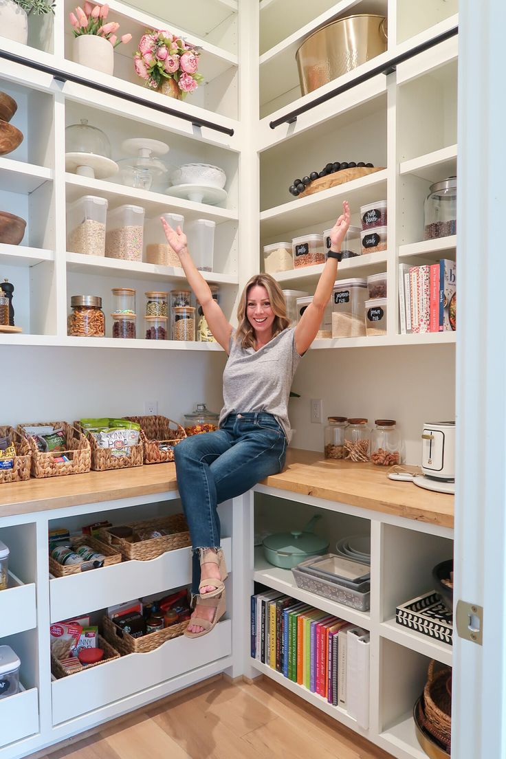 a woman sitting on top of a wooden shelf in a kitchen filled with lots of shelves