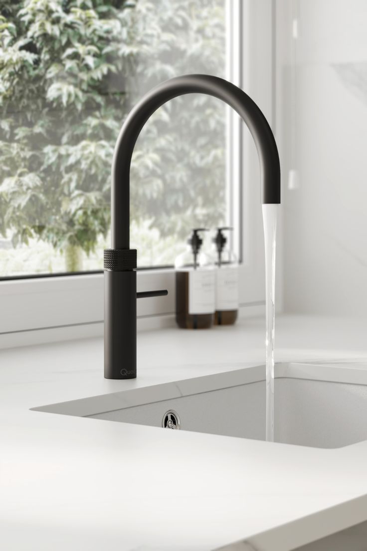 a black faucet running water from a kitchen sink in front of a window