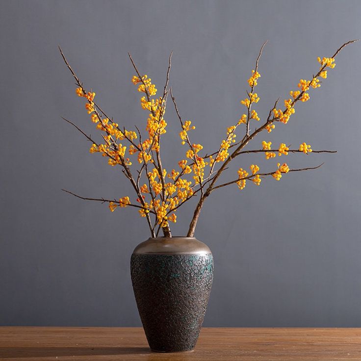 a vase filled with yellow flowers on top of a wooden table next to a gray wall