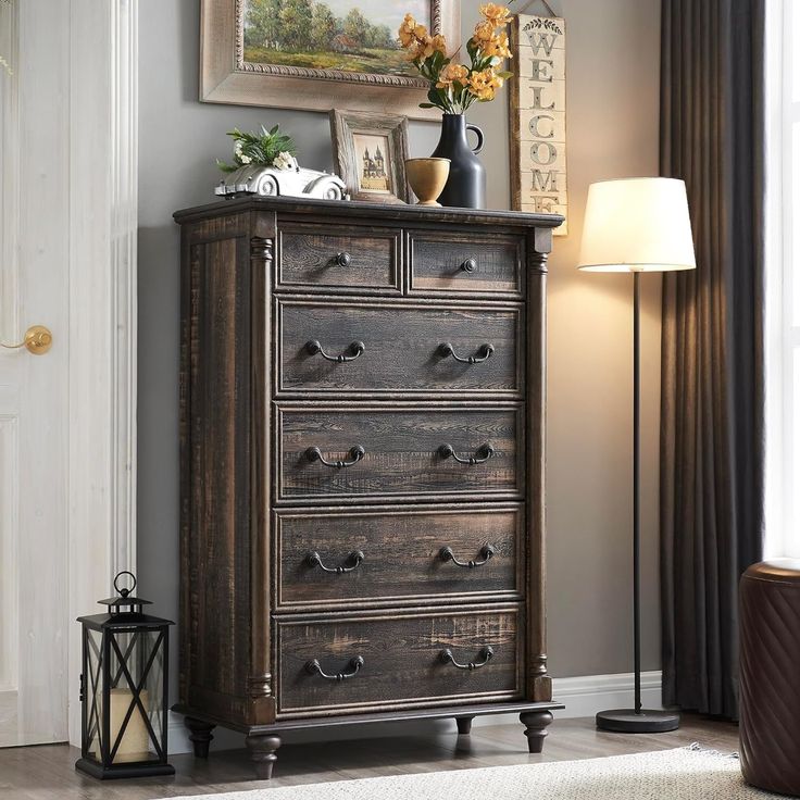 a dresser with drawers in a living room next to a lamp and pictures on the wall