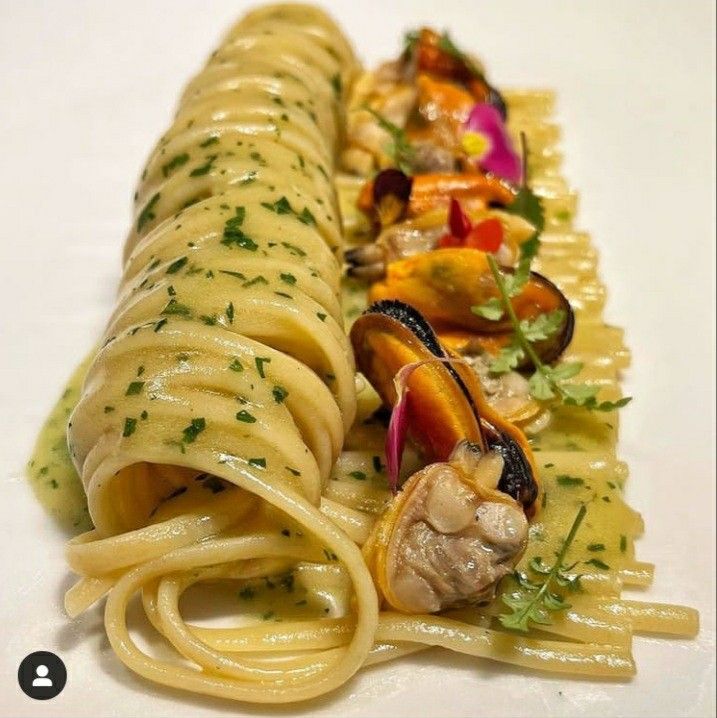 two pastas with sauce and vegetables are on a white tablecloth, one is cut in half