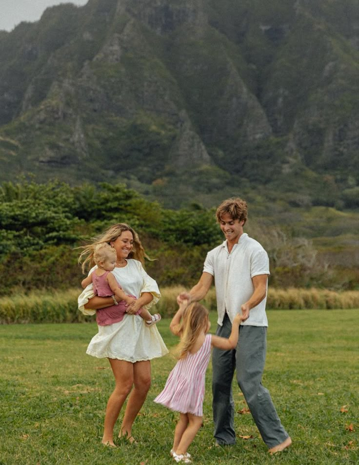 a man and two girls holding hands while standing in the grass with mountains behind them