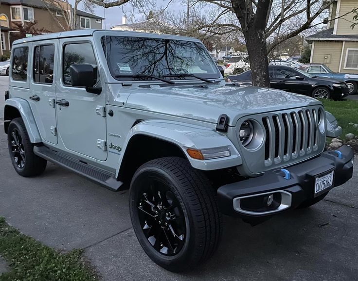 a silver jeep parked on the side of a road next to a tree and houses