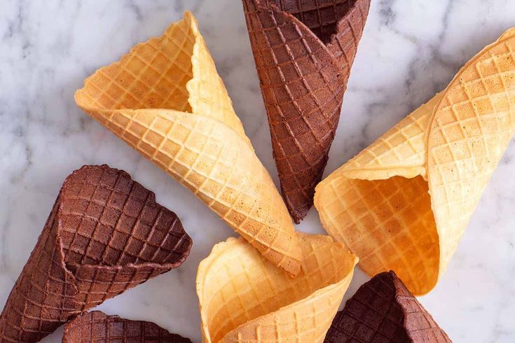 four cones of chocolate ice cream on a marble counter top with one cone cut in half