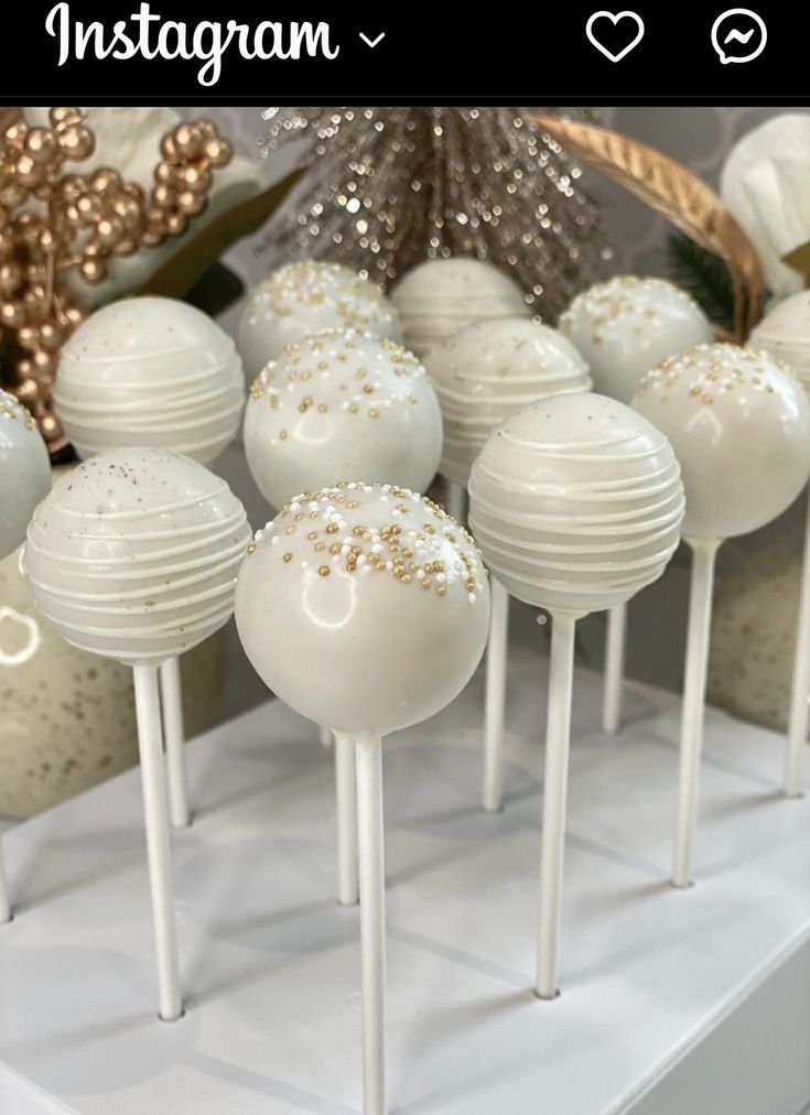 white cake pops with gold sprinkles are on display in front of christmas decorations