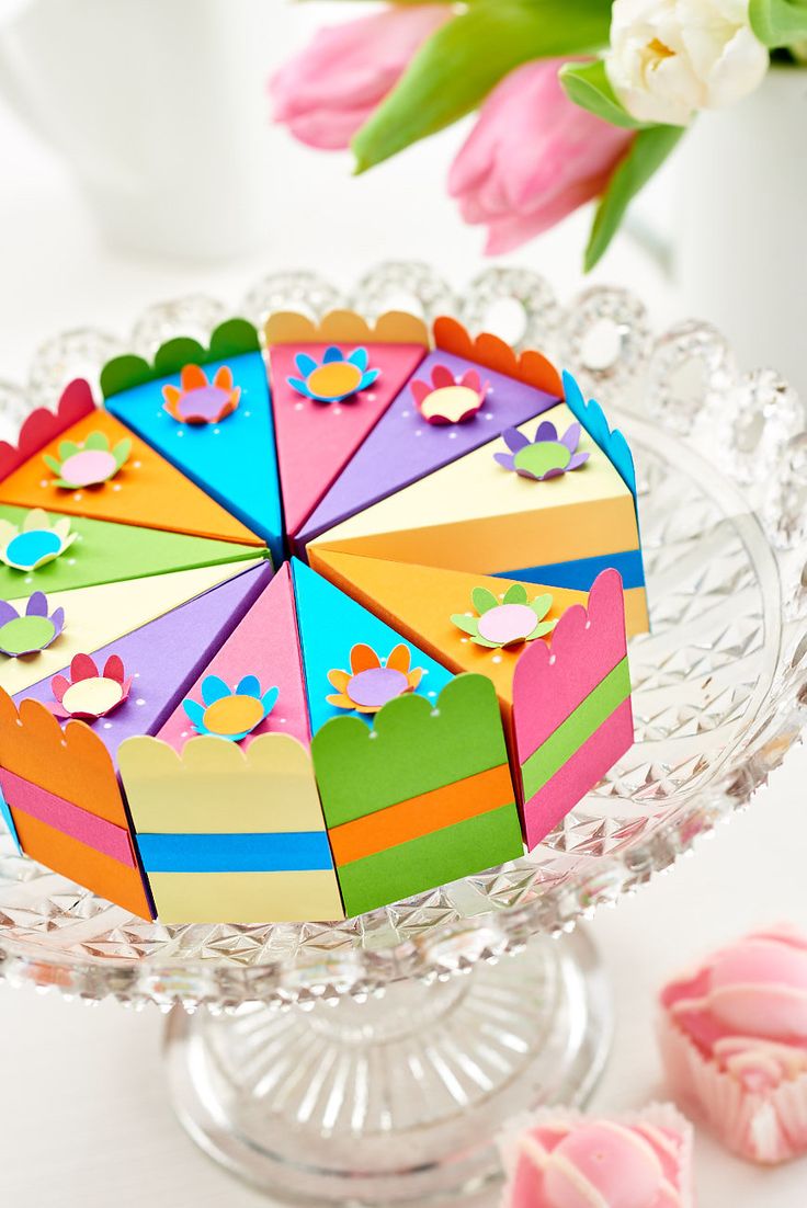 a colorful cake on a glass plate with flowers in the background