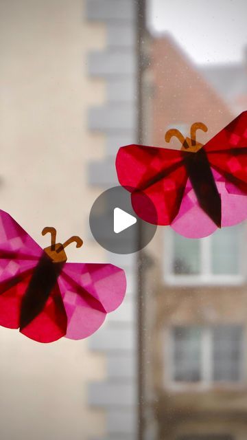 two pink paper butterflies are hanging from a window sill in front of a building