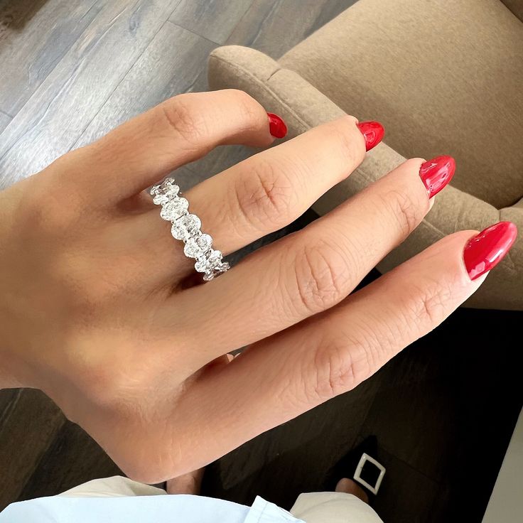 a woman's hand with red nail polish holding an engagement ring in her left hand