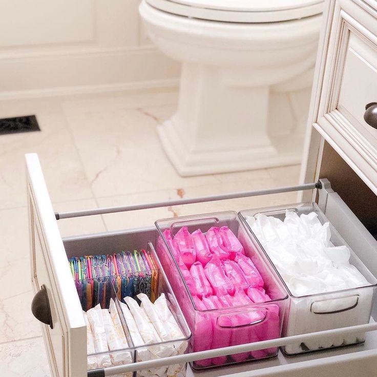 two trays filled with pink and white items in front of a toilet on a bathroom floor