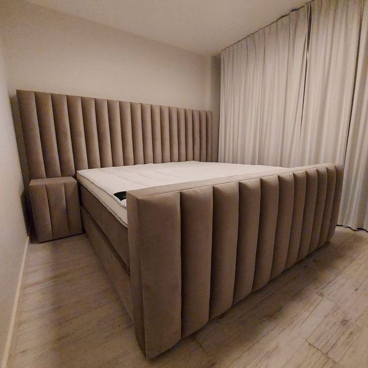 a bed that is in the middle of a room with wooden flooring and curtains