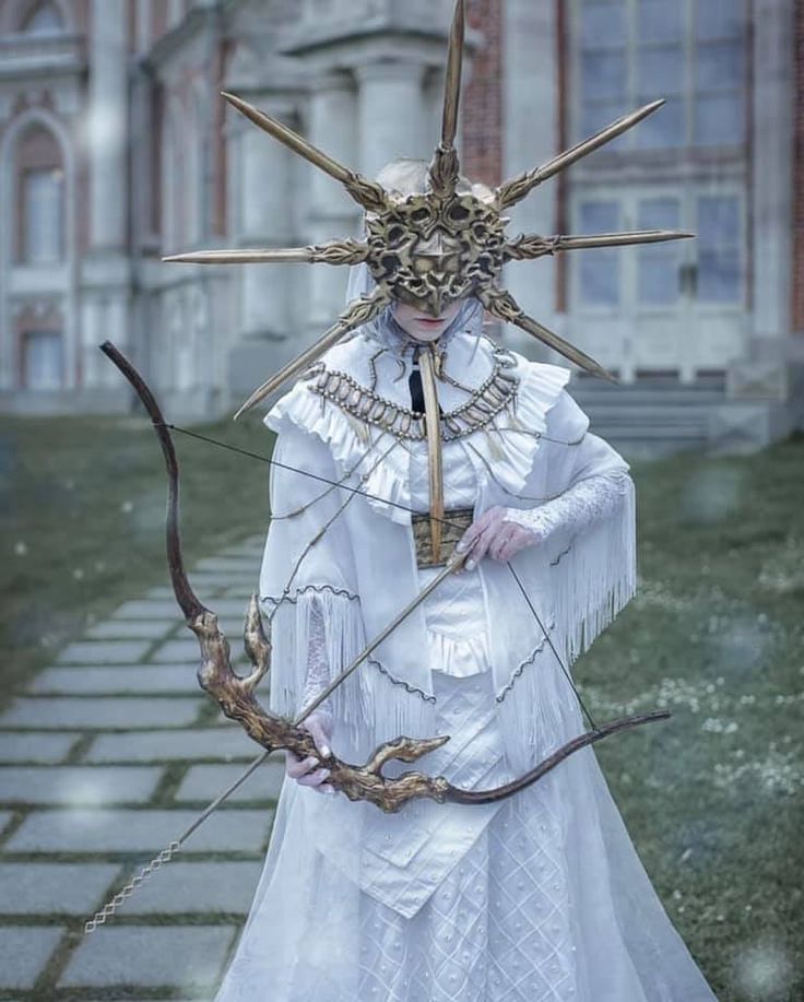 a woman dressed in white holding an arrow and wearing a mask with horns on her head