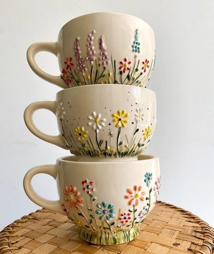 three coffee cups are stacked on top of each other, with flowers painted on them