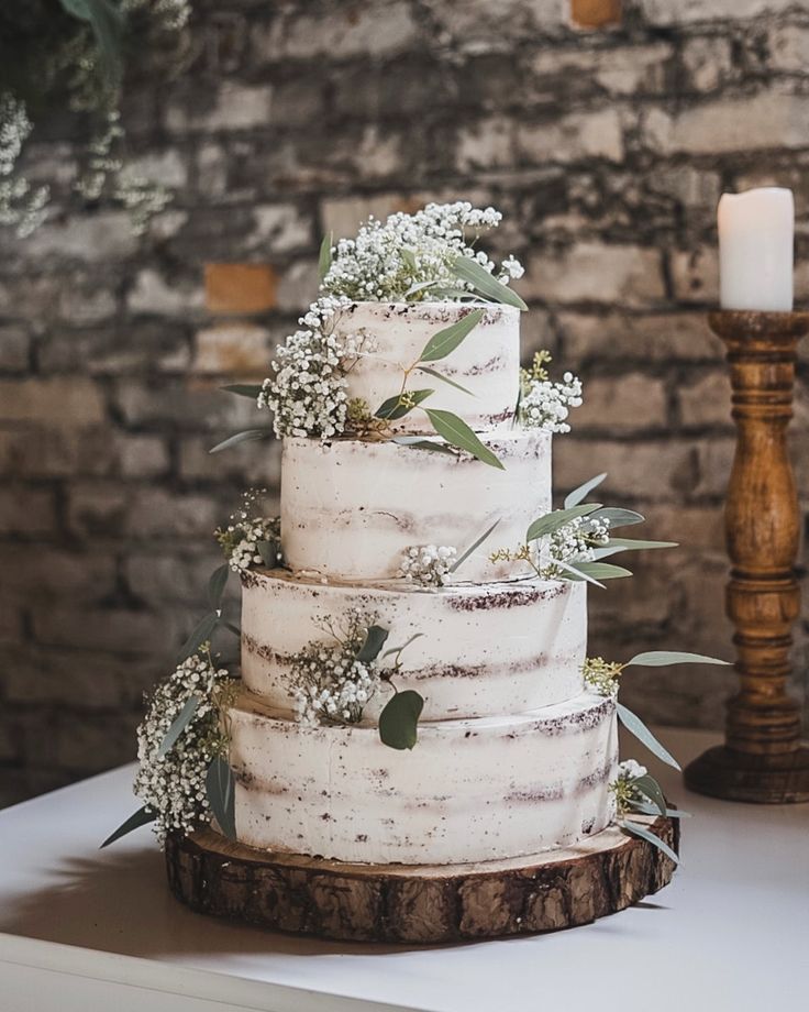 a wedding cake with white frosting and greenery sits on a table next to a candle