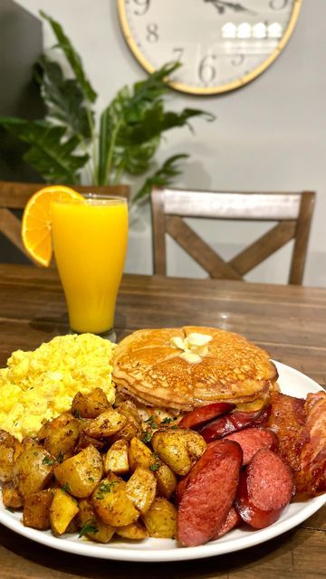 a breakfast plate with eggs, bacon, pancakes and hash browns on a table next to a glass of orange juice