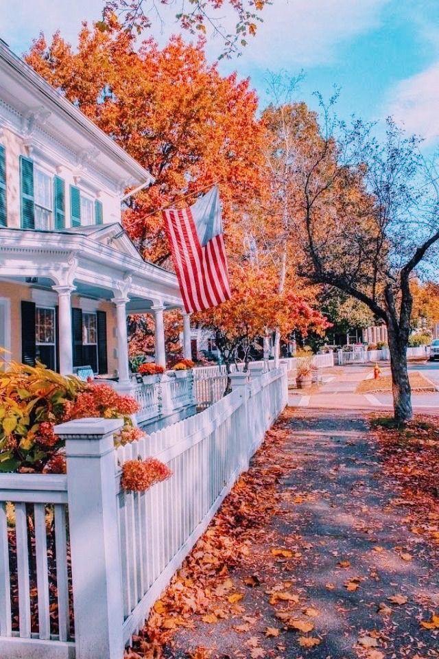 an american flag is hanging on the side of a white picket fence in front of a house