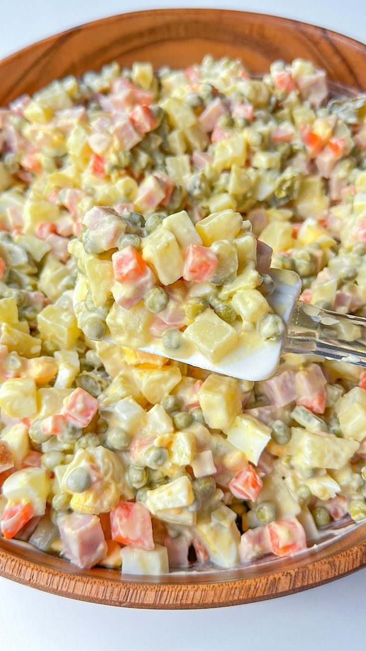 a wooden bowl filled with potato salad on top of a white tablecloth next to a fork