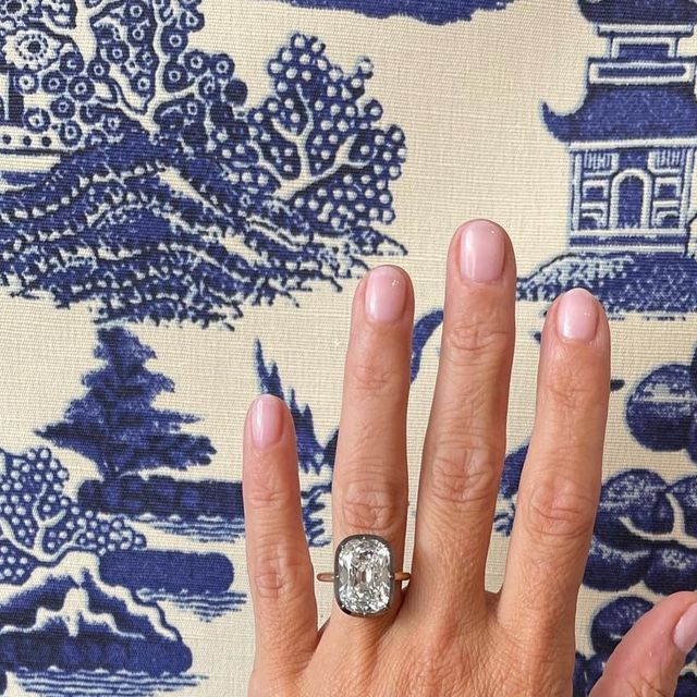 a woman's hand with a diamond ring on top of her finger, in front of a blue and white background