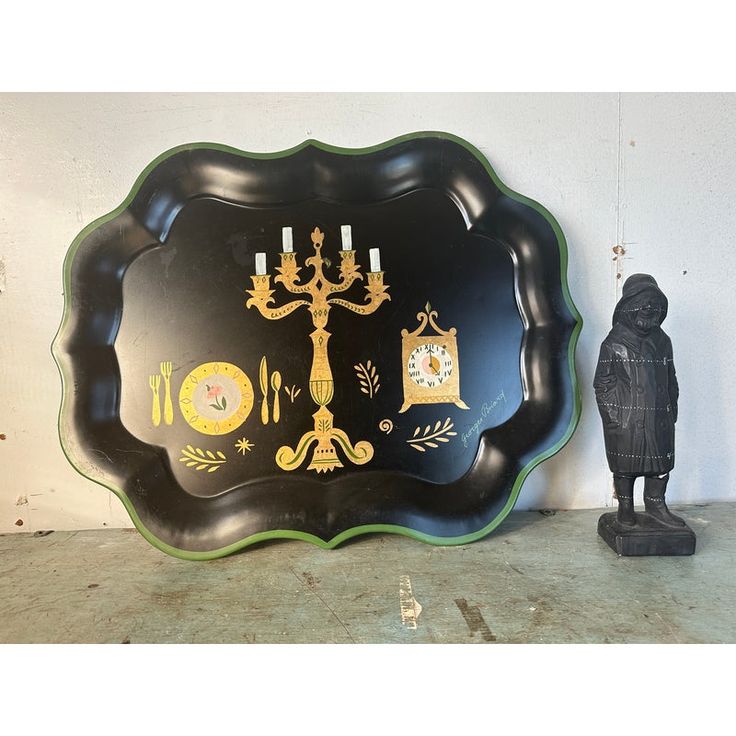 an ornate black and green tray with candles on it next to a small figurine