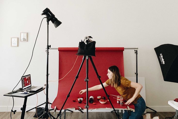 a woman sitting in front of a camera on a tripod next to a red backdrop