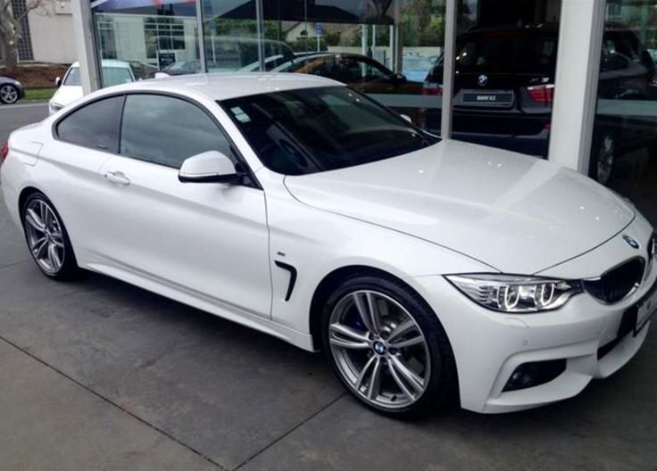 a white bmw car parked in front of a building next to other cars on the street