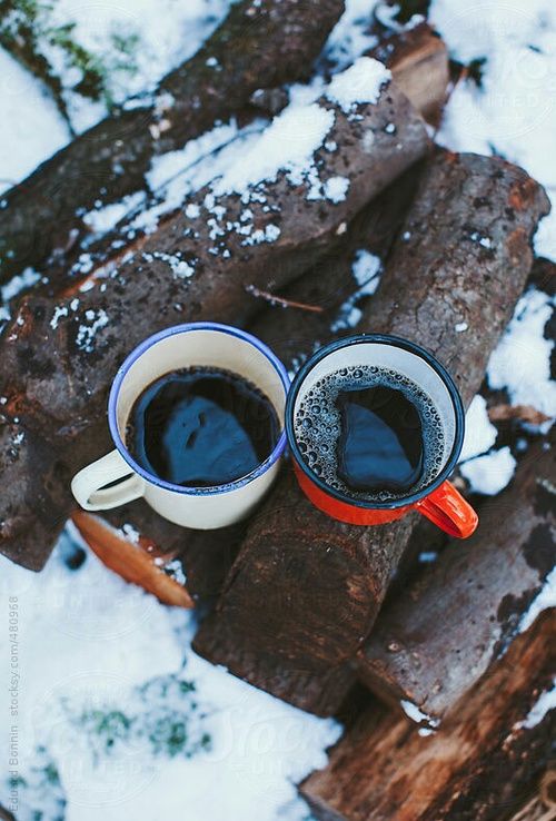 two cups of coffee sitting on top of each other in front of snow covered logs