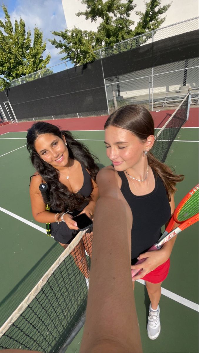 two young women standing on a tennis court holding racquets and smiling at the camera