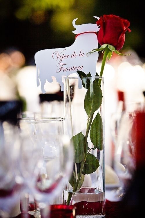 a red rose in a vase with water and wine glasses on the table at a wedding reception