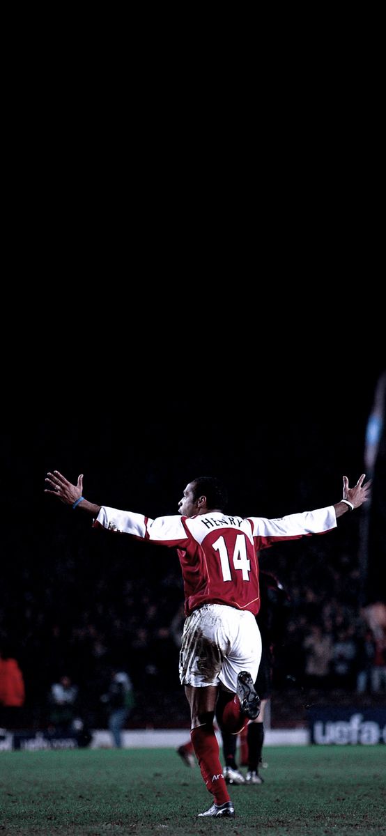 a soccer player with his arms outstretched in the air, on a field at night