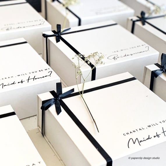 many white boxes with black ribbons tied around the edges and some flowers in each box