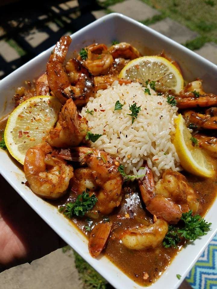 a white plate topped with shrimp and rice covered in sauce next to lemon wedges