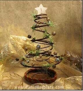 a small christmas tree made out of wire and wood with green leaves on top, sitting in a bowl