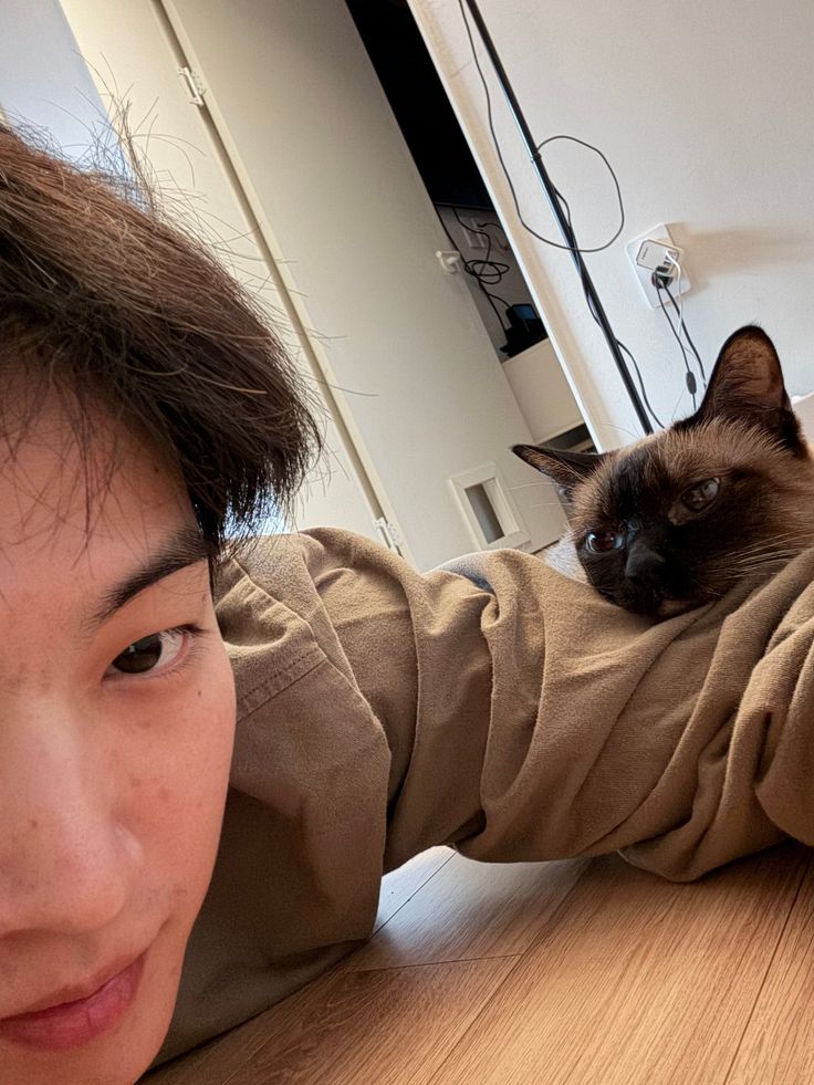 a person laying on the floor with a cat in their lap and looking at the camera