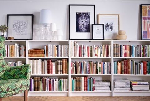 a room filled with lots of books on top of a white book shelf next to a green chair