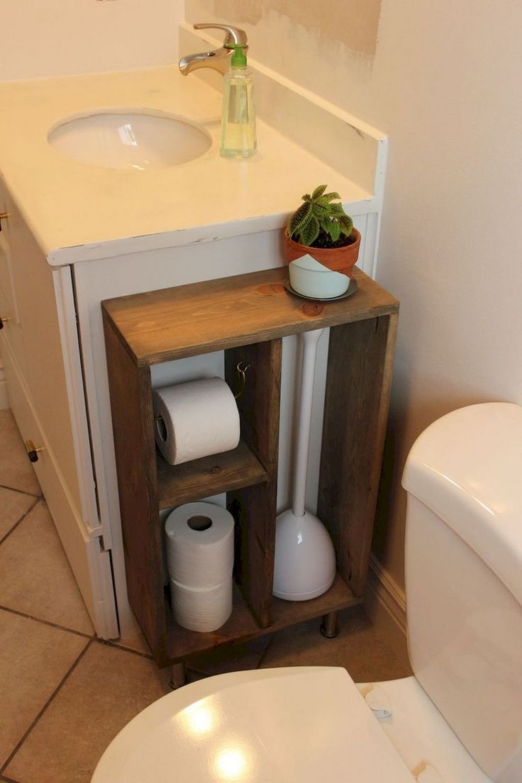 a white toilet sitting next to a wooden cabinet in a bathroom under a faucet